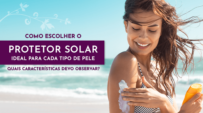 Mulher sorridente aplicando protetor solar no ombro em uma praia ensolarada, segurando uma embalagem laranja, com o mar ao fundo.